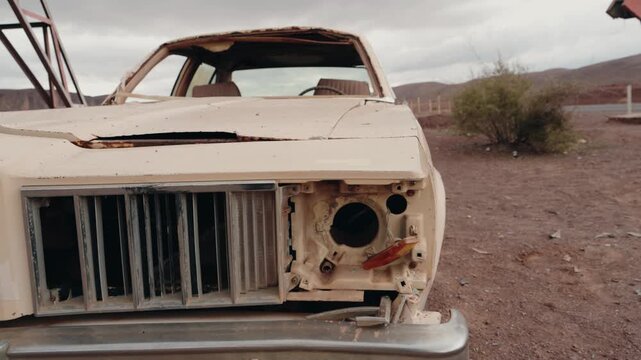 Abandoned car in the desert of Morocco. Old, rusty, and damaged vehicle left on the side of the road. The car's broken windows, missing headlight, and damaged hood tell a story of neglect.