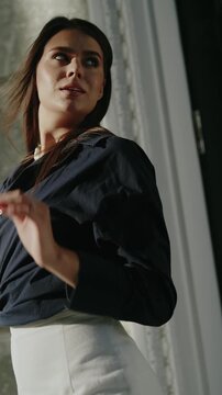 Confident businesswoman adjusts hair in modern office. Professional woman in stylish business attire exudes success and determination in corporate setting. Natural light emphasizes her poised demeanor