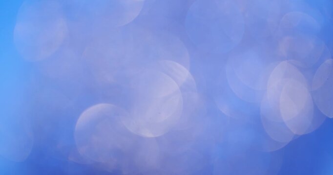 Abstract background of blurred blue and purple bokeh light circles shimmering and moving slowly, creating a magical and glittering effect for celebrations, parties, or festive events