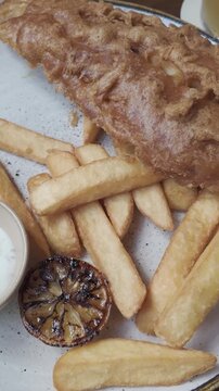 Delicious plate of classic fish and chips with a grilled lemon half and creamy tartar sauce, a popular and traditional British meal served in a pub or restaurant in the United Kingdom