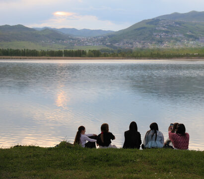 back rear view of group of people family friends sitting on grass floor closely and looking, girls gathering sitting backward to camera near Lisi lake in the evening Tbilisi Georgia Mountain around