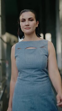 A confident woman in a stylish blue dress walks through a modern city passage. She exudes professionalism and style, embodying urban chic. Her determined stride suggests purpose and success.