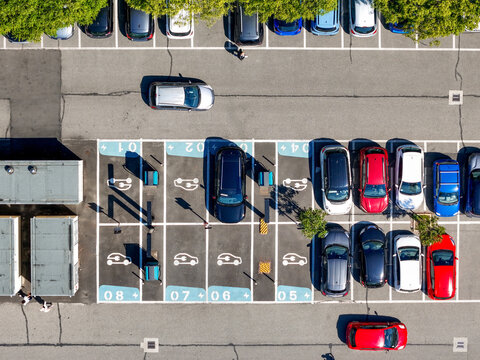 Aerial view of an electric vehicle charging station with parked cars and EV symbols on the asphalt in Turin, Piedmont, Italy.