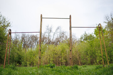 Fototapeta premium Symmetrical view of rusted metal bars in a natural setting. Abandoned exercise frames standing in a overgrown green field
