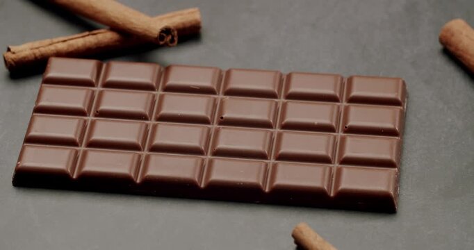 Delicious close-up of a chocolate bar with cinnamon sticks on a dark background. Perfect for dessert, indulgence, and gourmet themes.