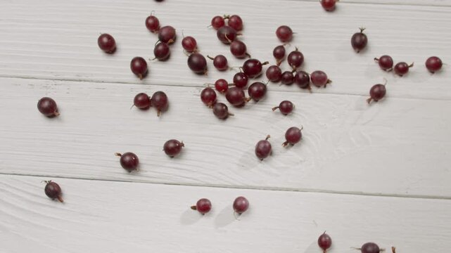 A collection of fresh red gooseberries spread across a white wooden background. Ideal for themes of food, nutrition, and freshness. Fresh Red Gooseberries Scattered on White Wooden Surface