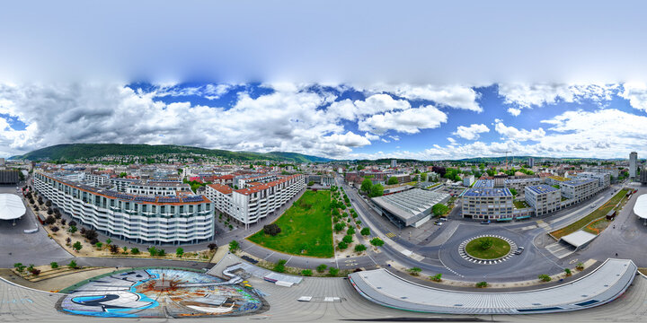 Aerial view of modern residential complexes, green urban spaces, and a roundabout under a dramatic cloudy sky in Biel Bienne, Canton of Bern, Switzerland.