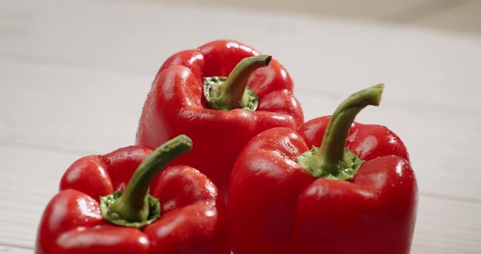 Close-up of three fresh red bell peppers on a white wooden background. The peppers are vibrant, juicy, and healthy, ideal for fresh food and healthy eating concepts. Fresh Bell Peppers Close-Up