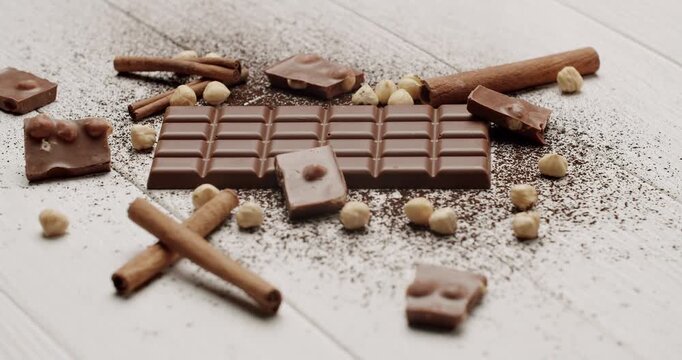Milk chocolate bar with hazelnuts and cinnamon sticks on a rustic white wooden table sprinkled with cocoa powder. Perfect for dessert, snack, and sweet moments. Delicious Milk Chocolate Bar, Hazelnuts