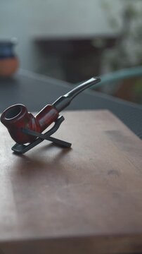 Primer plano vertical de pipa de madera cl&aacute;sica sobre mesa de madera con fondo desenfocado y luz natural de d&iacute;a.