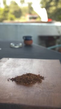 Primer plano vertical de tabaco suelto picado sobre mesa de madera r&uacute;stica con fondo desenfocado y luz natural.