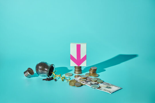 Fallen light bulb with sprout, euro coins and 100 dollar bill with down arrow sticker on turquoise background, failed mixed currency investment concept, copy space