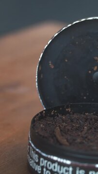 Primer plano de tabaco masticable oscuro en envase circular abierto, formato vertical 4K.