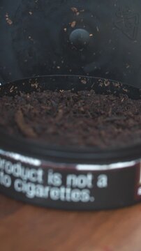 Primer plano de tabaco masticable oscuro en envase circular abierto, formato vertical 4K.