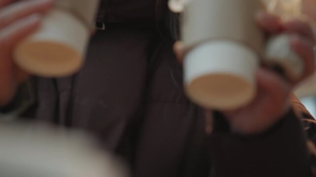 Winter market white woman holding coffees, college student balancing two takeaway cups, knitted beanie, round glasses, brown puffer coat, cardboard sleeves, closeup lids, cold window light, festive
