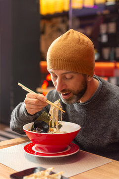 Young bearded man eating ramen at restaurant table