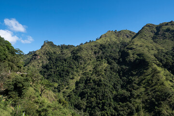 Obraz premium View from below of Little Adam's Peak in Ella, Sri Lanka. Majestic green mountain slopes and tropical forest under a blue sky.