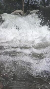 Slow Motion of Powerful blue waves splash over river rocks and white foam into the wet landscape of the liquid ocean
