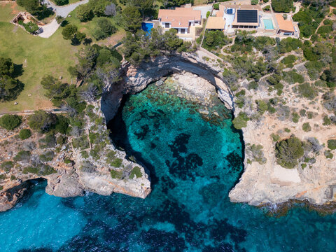 Aerial view of the turquoise waters of Cala Llombards cove surrounded by rocky cliffs and coastal villas Cala Llombards, Illes Balears, Spain.