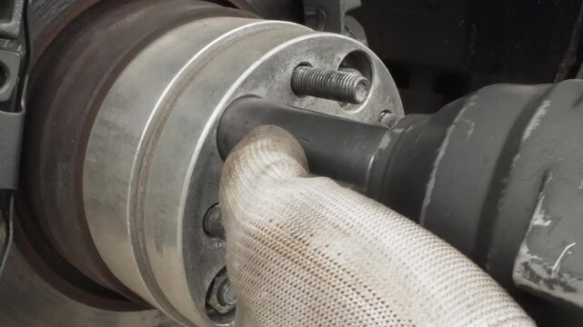 Closeup gloved mechanic disassembling wheel hub with socket and ratchet, rusted studs and brake drum visible workshop scene shows heavy vehicle axle, precise removal of studs, hands in protective