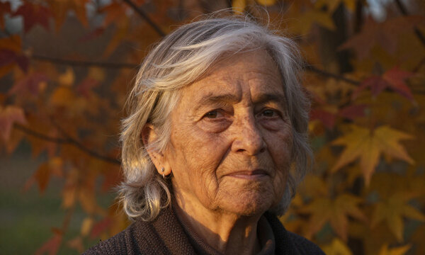 elderly woman wisps silver hair warm earthy complexion stands amidst autumnal foliage bathed soft golden