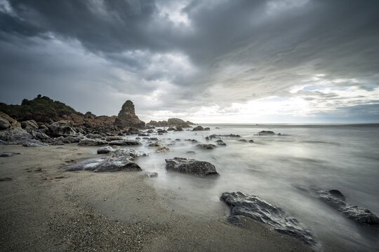 Rocky coast, rocks on the beach, dark rain clouds, long time exposure, West Coast, South Island, New Zealand