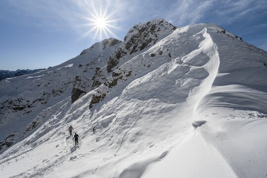 Snow cornices at an embrasure, hikers in the snow at Roggentalsattel, hiking trail to Ammergauer Hochplatte, sun star, in autumn, Ammergau Alps, Bavaria, Germany