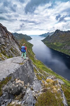 Fjord and mountains, view from mountain Barden, young hiker standing at a cliff, Senja, Norway