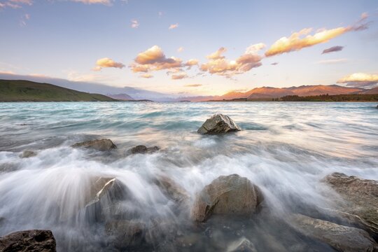 Stones on shore, lake with sunset swell, long time exposure, Lake Tekapo, Canterbury, South Island, New Zealand