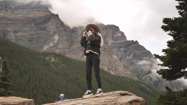 Young girl is taking a photo of a Majestic view of the turquoise Moraine Lake and the Valley of the Ten Peaks, Banff National Park, Alberta, Canada. Road trip in Canada. Rocky mountains. 4k footage.