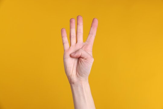 Woman showing number four with fingers on yellow background, closeup