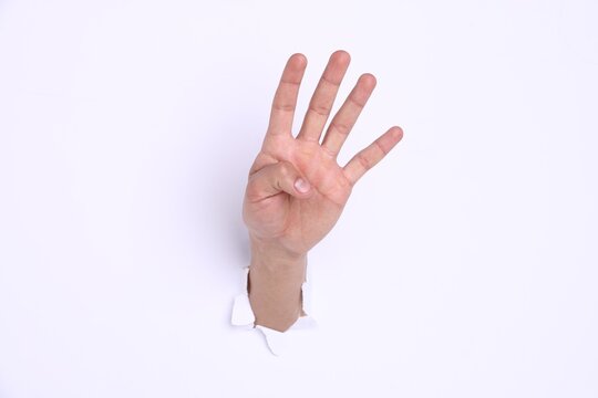 Man showing number four with fingers through hole in white paper, closeup