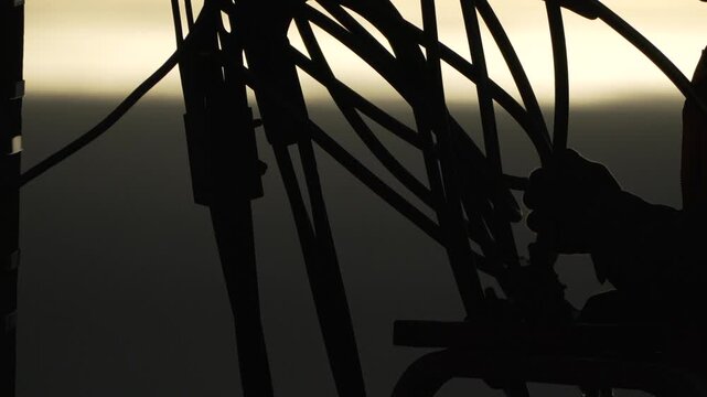 Worker, silhouette, industry, technician operating complicated cable machinery at dramatic sunrise or sunset background.