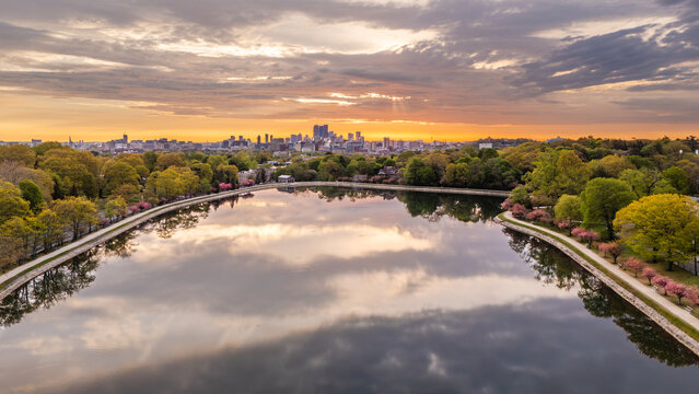 Aerial view of Brookline Reservoir reflecting a colorful sunrise sky with the Boston skyline on the horizon and spring trees along the shore Brookline, Massachusetts, United States.