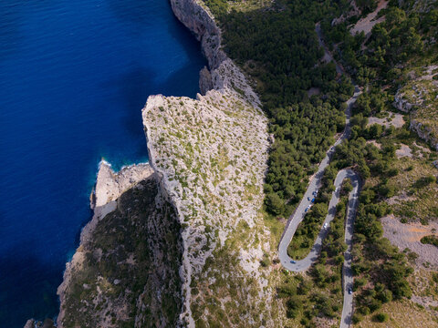 Aerial view of the winding road at Cap de Formentor with hairpin turns along steep rocky cliffs overlooking the deep blue sea in Balearic Islands, Spain.
