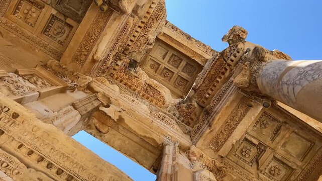 Close-up view of the Library of Celsus in ancient Ephesus, Turkey. Detailed Roman columns, marble facade and ornate carvings under clear blue sky.