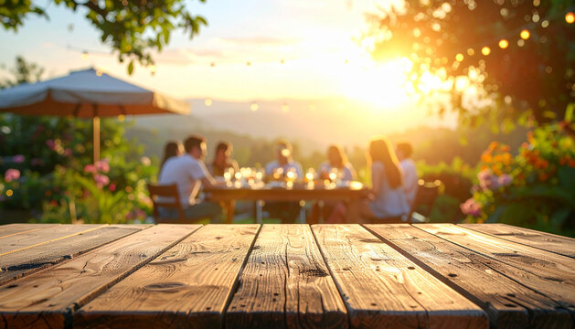 Wooden table top offering copy space with a blurred festive garden party and friends in the background during a golden sunset for outdoor event promotion and summer celebration invitations