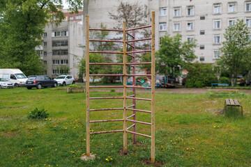Peeling metal ladder structure for children in a city park area with a large apartment block and green vegetation © WoodHunt