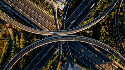 Aerial view capturing a complex motorway interchange, showing numerous roads and elevated highways intertwining with light traffic moving through the green urban infrastructure © Nasos Zovoilis
