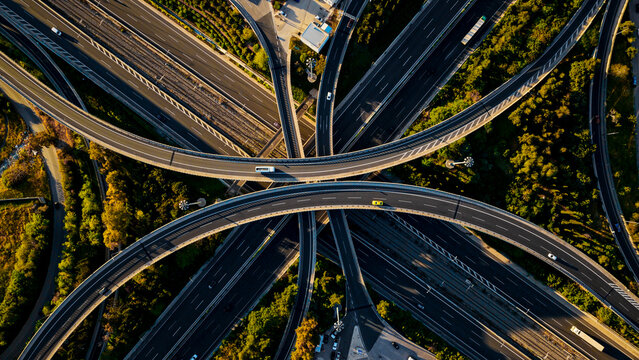 Aerial view capturing a complex motorway interchange, showing numerous roads and elevated highways intertwining with light traffic moving through the green urban infrastructure
