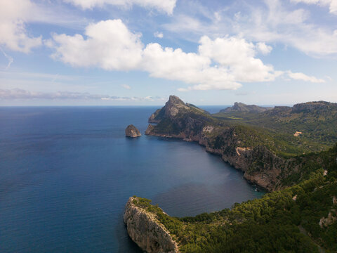 Aerial view of Cap de Formentor featuring dramatic limestone cliffs, lush green vegetation, and the deep blue Mediterranean Sea under a cloudy sky Balearic Islands, Spain.