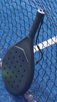 Vertical video: Camera pulling back revealing padel racket on net at blue court, green ball resting