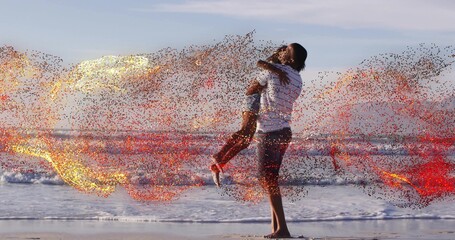 Obraz premium Lifting father holding daughter over wet sand at shoreline, striped shirt, sneakers, sparks