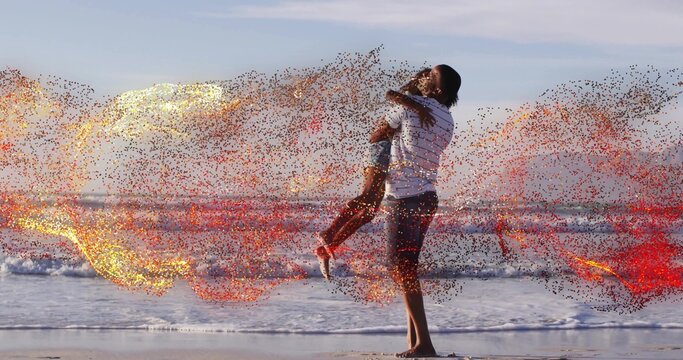 Lifting father holding daughter over wet sand at shoreline, striped shirt, sneakers, sparks