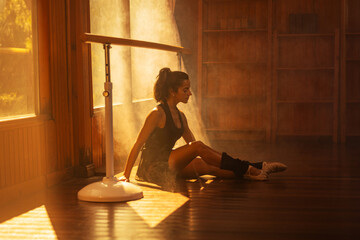 Ballerina in black sportswear practicing at a barre in a sunlit wooden studio. © Mike Orlov
