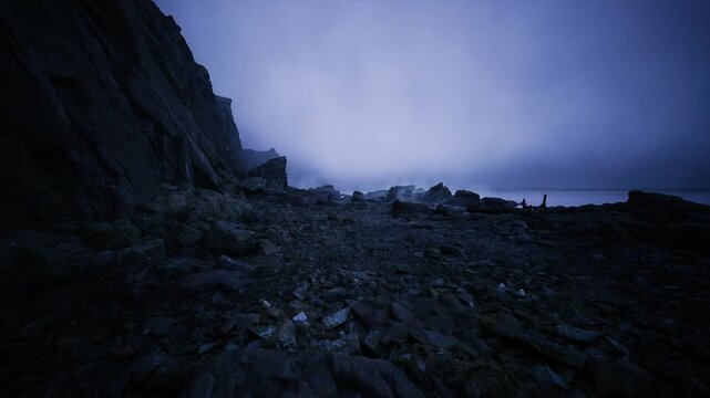 Twilight rocky shoreline under thick fog, scattered rusted beams and weathered stones suggest abandoned coastal settlement, silent driftwood and tide lines,