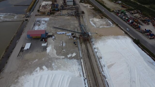 Aerial wide shot of salt factory warehouses beside highway and lagoons