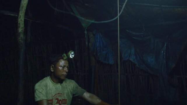 Manual oil worker with a headlamp operating a makeshift rig in an unregulated oil field in Myanmar