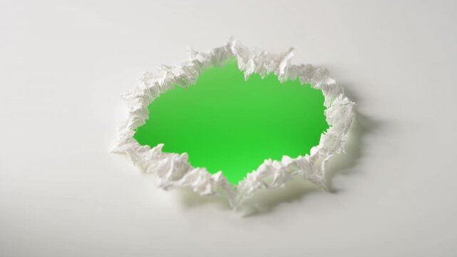 A torn hole reveals green through ripped paper on a plain surface