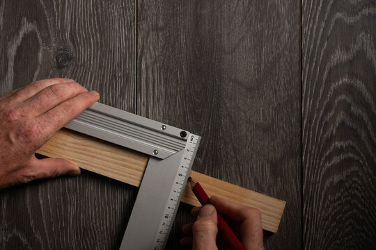 Marking wooden plank with carpenter square and red pencil on dark wood background